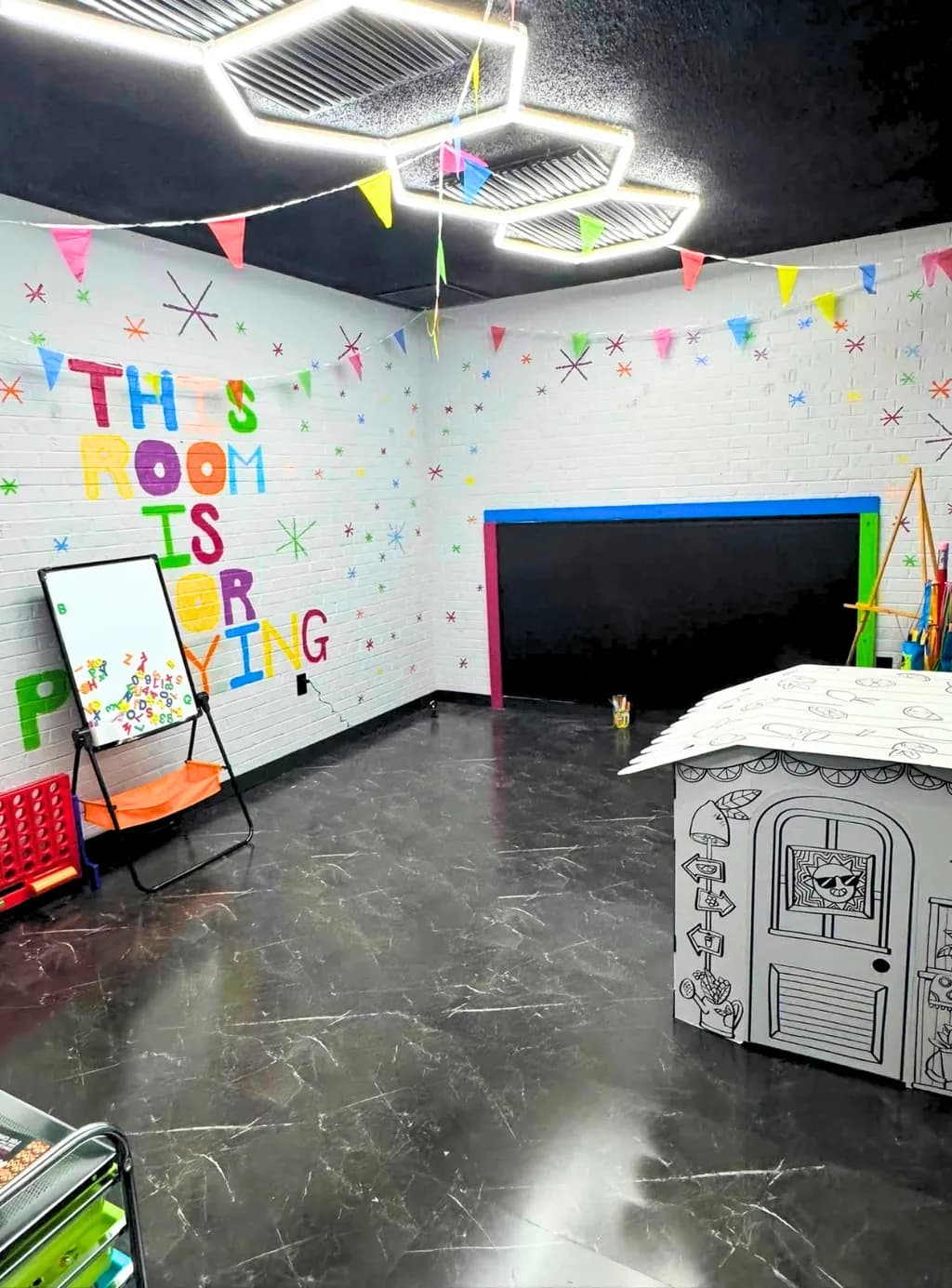 Craft room with a colorful lettered wall, whiteboard easel, and a cardboard playhouse.